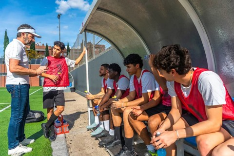 Soccer coach talking and giving instructions to his diverse team of young male athletes sitting on