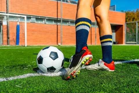 Female soccer player's legs and feet are positioned near a soccer ball on a green artificial turf