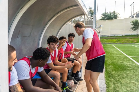 Youth soccer coach discussing strategy with his multiethnic male team members on the bench of a