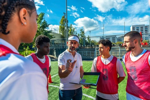 Soccer coach explaining game strategy to a diverse group of male players on a green artificial turf