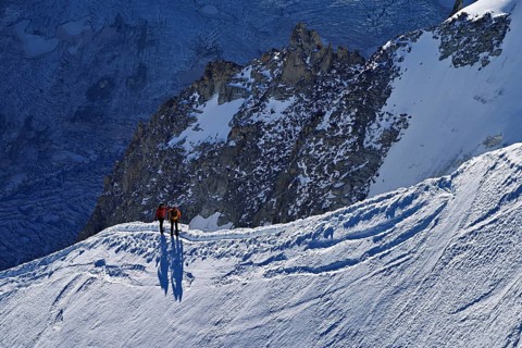 Two ascended mountaineers run across a snow-covered mountain ridge, Aiguille du Midi,