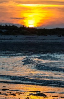 Sunset on a quiet beach with soft light on the waves, wet beach at low tide, dunes in the