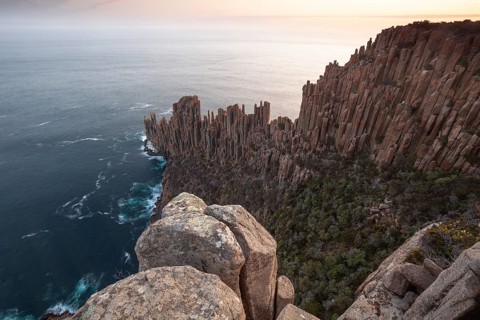 Long exposure shows sunset over the cliffs of Cape Raoul. Golden light hits the sea and colors the