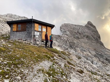 Two mountaineers in front of the Wildalmkirchl bivouac, in the background the summit of