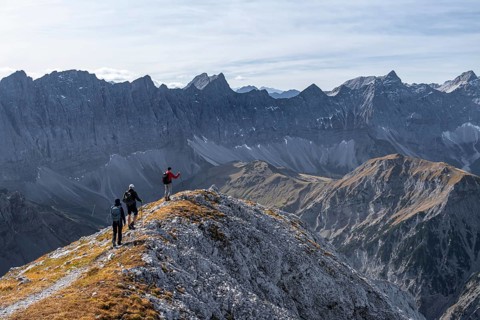 Hikers on the summit ridge of the Gamsjoch, behind rock faces of the Laliderer Spitze, eastern