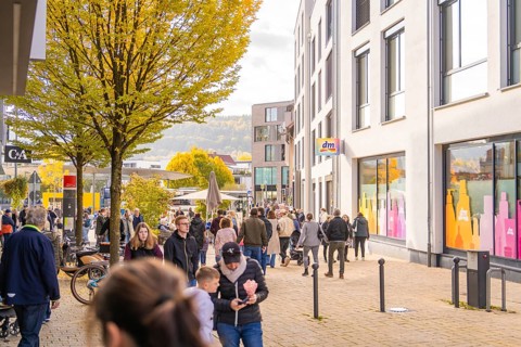 Busy shopping street in autumn, people strolling between modern buildings and colorful shops,