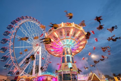 An illuminated chain carousel and Ferris wheel at night at a funfair, people swinging on chains,