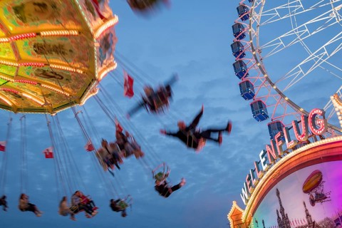 An illuminated chain carousel turns at night at a funfair, with floating people and colourful