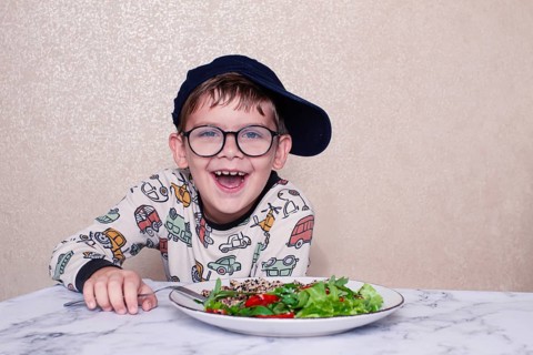 Child reacts dramatically to a salad served on a marble table at home during lunchtime, A little