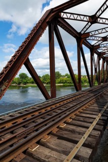 Railroad tracks leading to old rusted Terrebonne Pratt truss railroad bridge over Des Mille-Iles