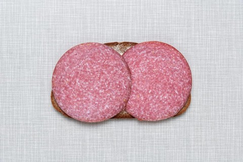 Top shot of a slice of bread smeared with margarine and topped with salami on a white Resopal plate