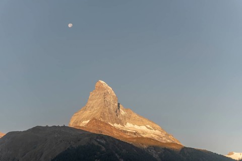 The iconic Matterhorn stands high above a clear evening sky illuminated by a bright moon. This
