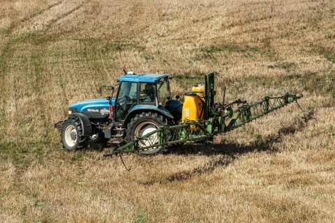 Tractor spreading fertilizer on harvested stubble field in Ystad municipality, Skåne county,