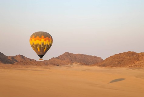 The hot-air balloon above an arid plain and isolated mountain ridges at the edge of the Namib
