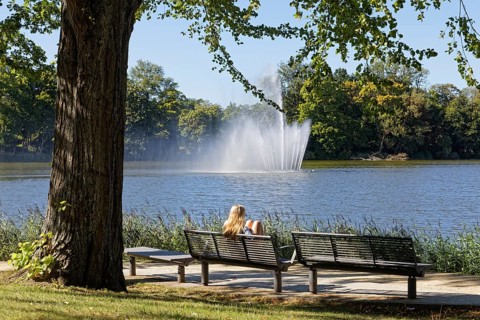Blonde woman on park bench looking at fountain in Knieperteich Stralsund, Mecklenburg-Vorpommern,