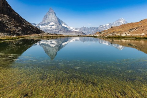 The sharp peak of Matterhorn rises majestically above a serene alpine lake, reflecting perfectly on
