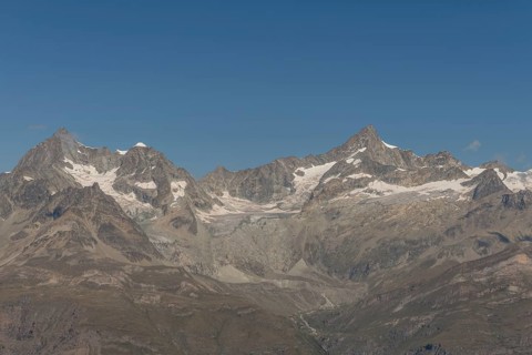 Majestic mountain peak rises prominently against a vibrant blue sky, surrounded by rocky terrain