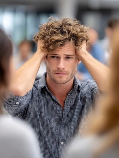 A young man with his hands to his ears, annoyed by an argument or noise in the background,
