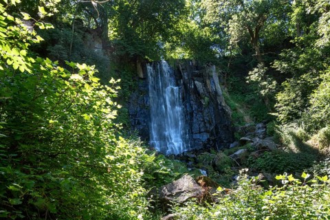 Vaucoux waterfall cascades gracefully over dark rocks, surrounded by lush greenery, Auvergne
