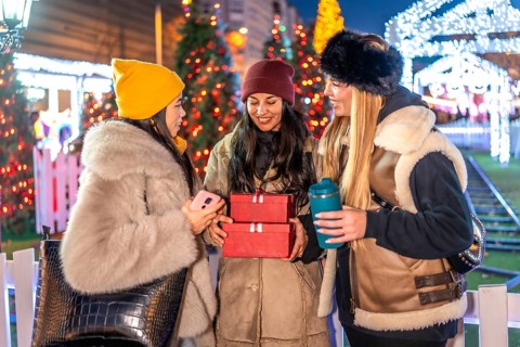 Three friends enjoying christmas time together, holding christmas gifts and a reusable cup at the