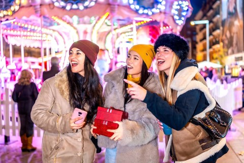 Three happy female tourists holding christmas gifts pointing at something at the christmas market