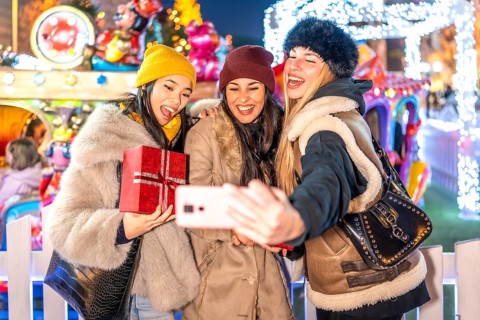 Three happy female friends taking a selfie with a smartphone at a christmas market amusement park,
