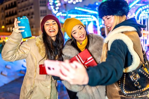 Three happy female friends are taking a selfie with a christmas gift at a christmas market,