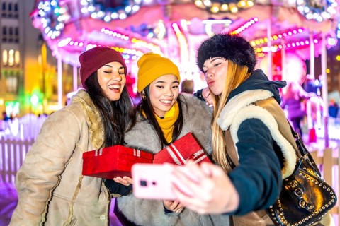 Three cheerful multi ethnic women taking a selfie with christmas presents at the christmas market