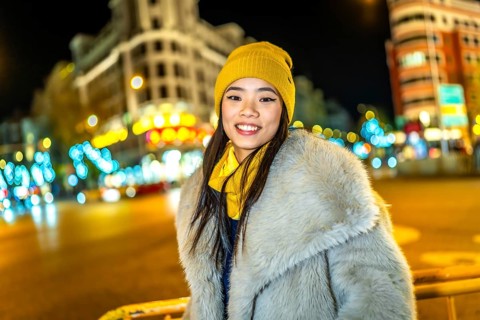 Asian woman wearing cozy winter clothes, smiling and enjoying the vibrant christmas lights
