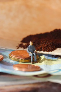 Miniature figure of a man sitting on coins and banknotes, ground coffee in a filter bag in the