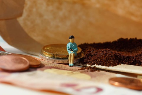 Miniature figure of a woman sitting on coins and banknotes, ground coffee in a filter bag in the