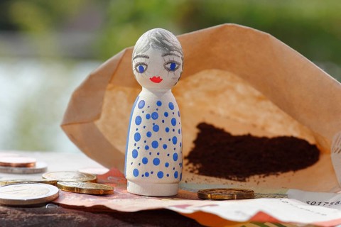 Pretty female wooden cone figure with coins and banknote in front of filter bag with coffee North
