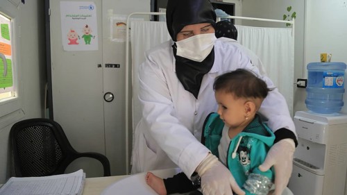 A doctor examining a refugee child for malnutrition in the camp using weight and height measurement