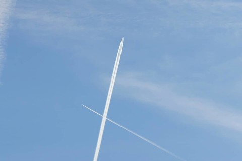 Two jet passenger aircraft with vapour trails or contrails flying in a blue sky crossing making a