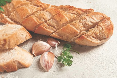 Garlic bread, baguette with garlic butter and herbs, on a light table, top view