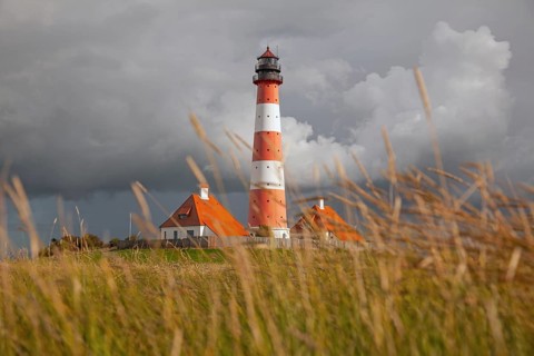 Illuminated Westerheversand lighthouse on the North Sea under dark storm clouds