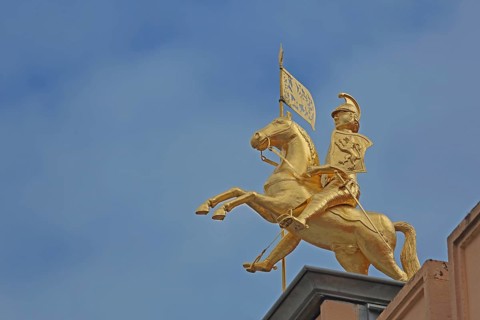 Golden equestrian figure with city coat of arms and flag, monument to city founder Henry the Lion,