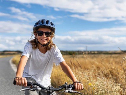 A girl with a bicycle helmet rides a bicycle and smiles friendly into the camera, AI generated, AI