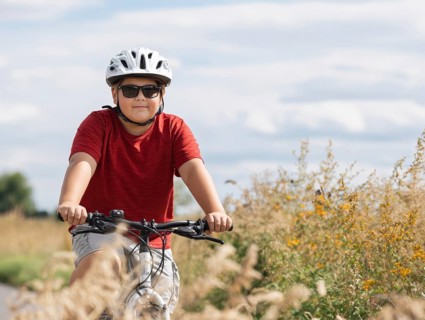 A boy with a bicycle helmet rides a bicycle and smiles friendly into the camera, AI generated, AI