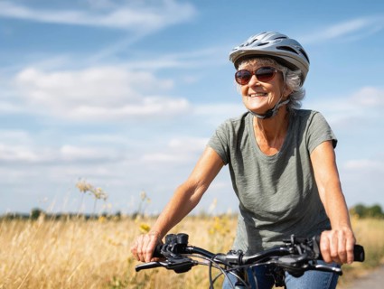 An elderly lady, a senior citizen with a bicycle helmet, rides a bicycle and smiles in a friendly
