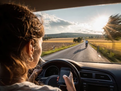 A car driver is dazzled by the sun and looks at her smartphone while driving, putting herself, the