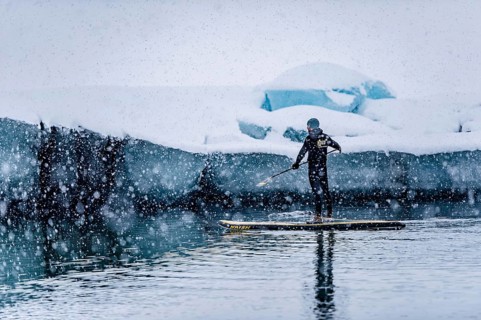 Man stand up paddling, snowfall, glacier lagoon Jökulsarlon at Vatnajökull, Iceland* Man stand up