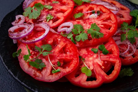 Freshly sliced tomatoes and red onions, garnished with herbs, on a black plate, summer salad, no