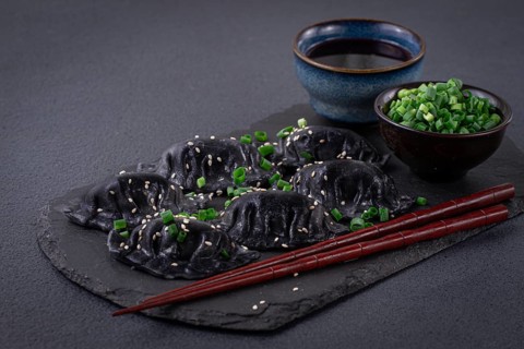 Japanese gyoza dumplings, made of black dough, black gyoza, with green onions and sauce, on a