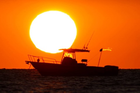 The sun rises behind a boat on the Costa Rei, a coastal stretch of the Italian Mediterranean island