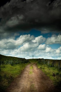 A winding dirt road leads the eye to a solitary cross. Cézallier, Auvergne Volcanoes Regional