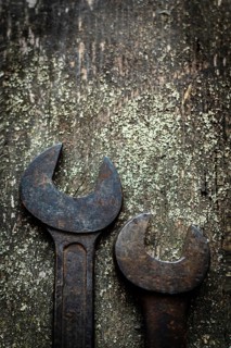 Two old, rusty wrenches rest side by side on a weathered wooden surface, highlighting their wear