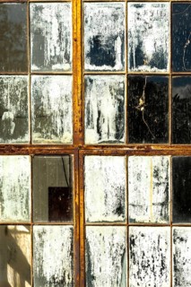 Cracked and peeling window panes reflect light and nearby objects, creating an atmosphere of