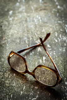 A pair of vintage glasses lies on a weathered wooden surface, enhanced by warm natural light