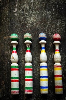 Four vintage wooden bowling pins with vibrant colors sit in a row on a rustic wooden surface,